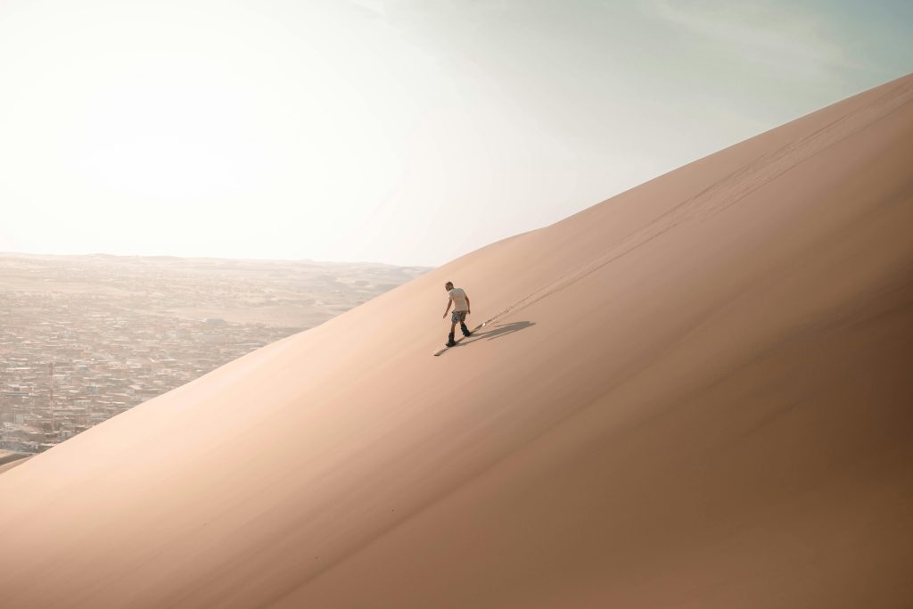 A man sandboarding down a vast dune in Huacachina, Perú, capturing the thrill of adventure in a stunning desert landscape.