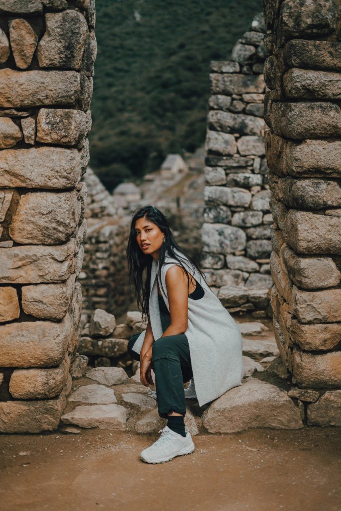 A young woman poses stylishly against ancient stone ruins in the outdoors of Peru.